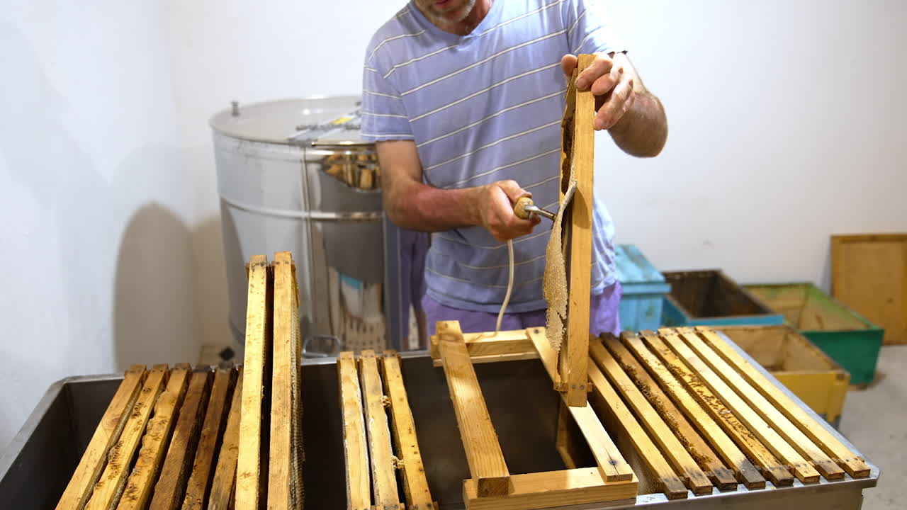 Beekeeper holding a frame and peels off the covers from the sealed cells. Preparation of frames for extracting honey.