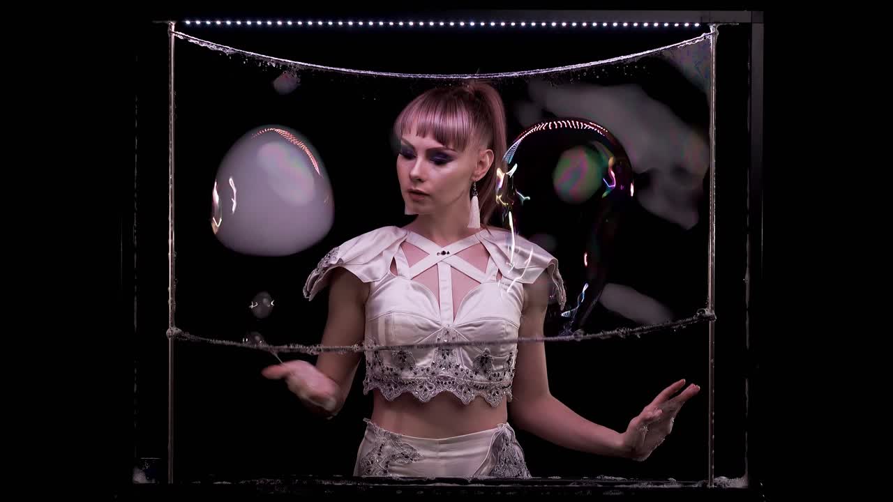 예쁜 소녀는 손가락을 사용하여 두 개의 큰 거품을 가지고 놀다가 연기로 하나에 연결합니다.