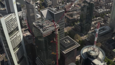 AERIAL:-Close-Up-View-of-Skyscraper-construction-site-in-Urban-environment-with-city-car-traffic-and-reflections-in-tower-at-sunny-day-in-Frankfurt-am-Main-Germany