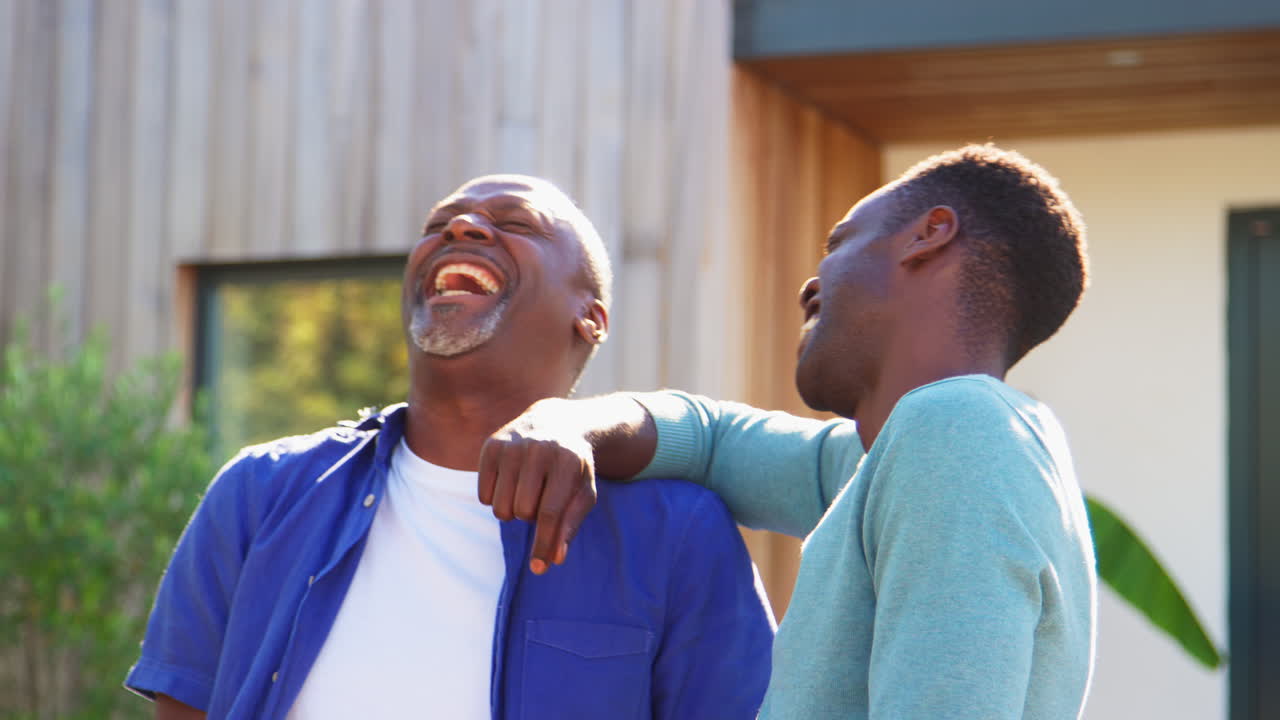 amoroso padre mayor con hijo adulto de pie fuera de la casa riendo juntos