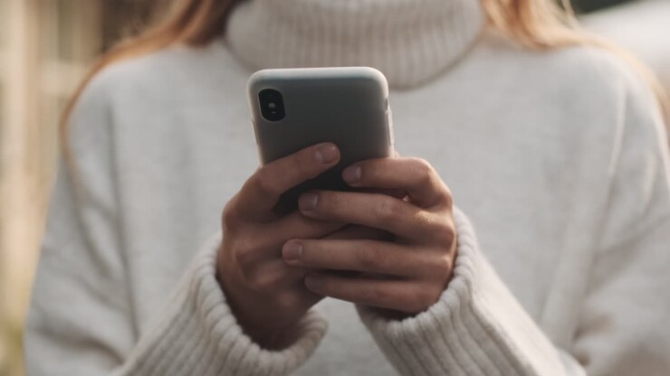 Caucasian female typing on smartphone outdoors.