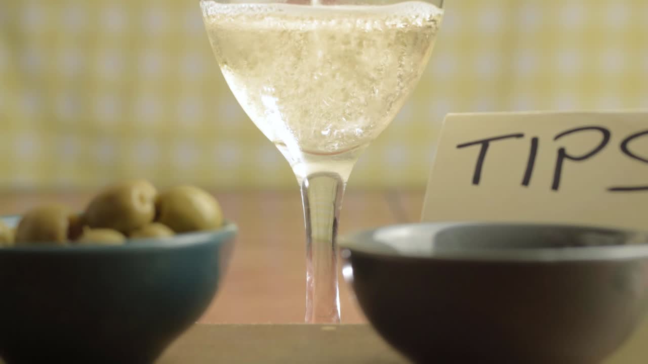 Tipping jar in cafe with white wine pouring in background close up shot