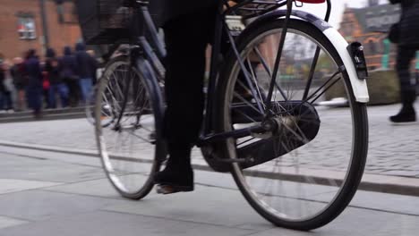 person peddles bicycle on city sidewalk toward and past camera, close up slow motion low view, copenhagen, denmark
