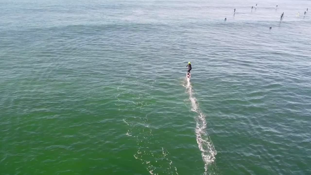 Aerial slow-motion view of a foil drive surfer heading out to catch ocean waves, gliding smoothly towards the horizon in middle of SUP