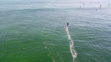 aerial slow-motion view of a foil drive surfer heading out to catch ocean waves, gliding smoothly towards the horizon in middle of sup