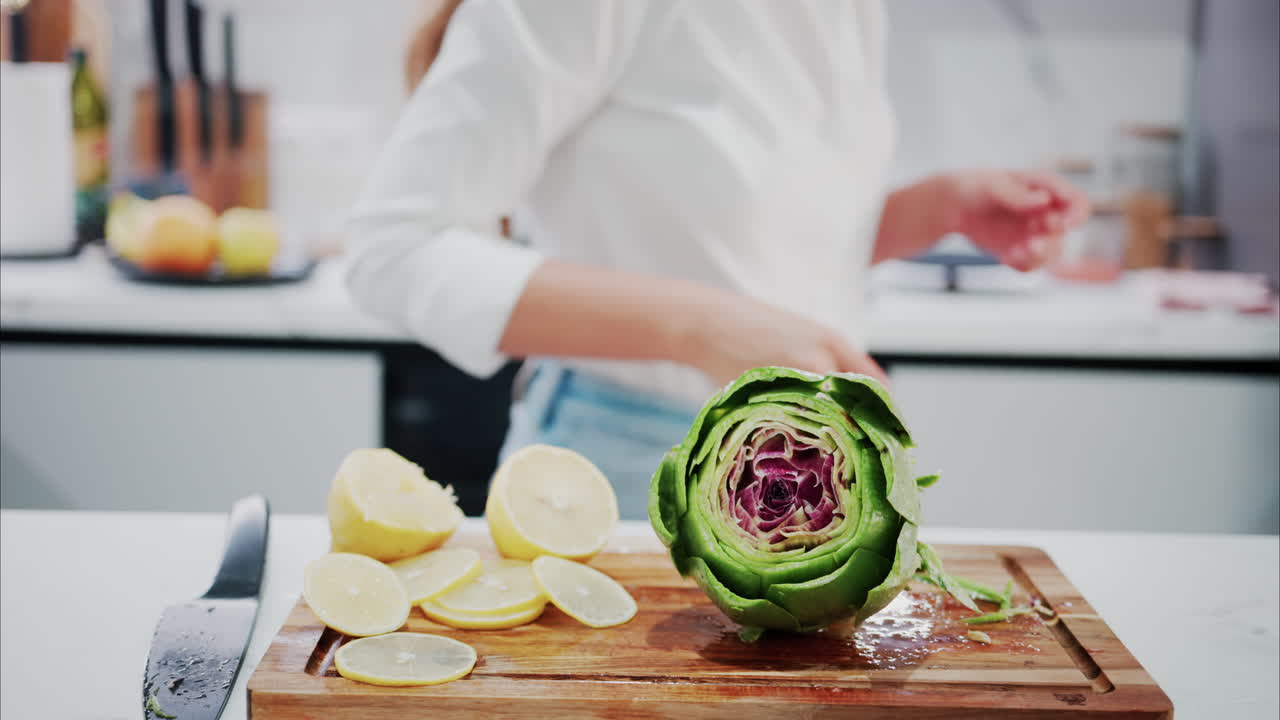 Woman squeezing lemon juice over an artichoke on a wooden cutting board