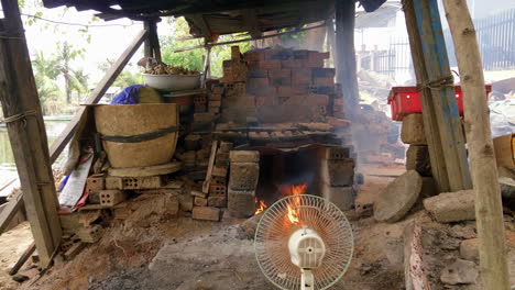 high wide view of raging wood fire in pottery kiln, fan blows fire and smoke, than ha hoi an vietnam