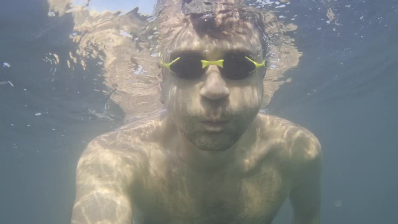 Uomo con occhialini da nuoto che esplora l'acqua limpida e blu. La luce del sole crea splendidi riflessi sulla superficie e sul corpo