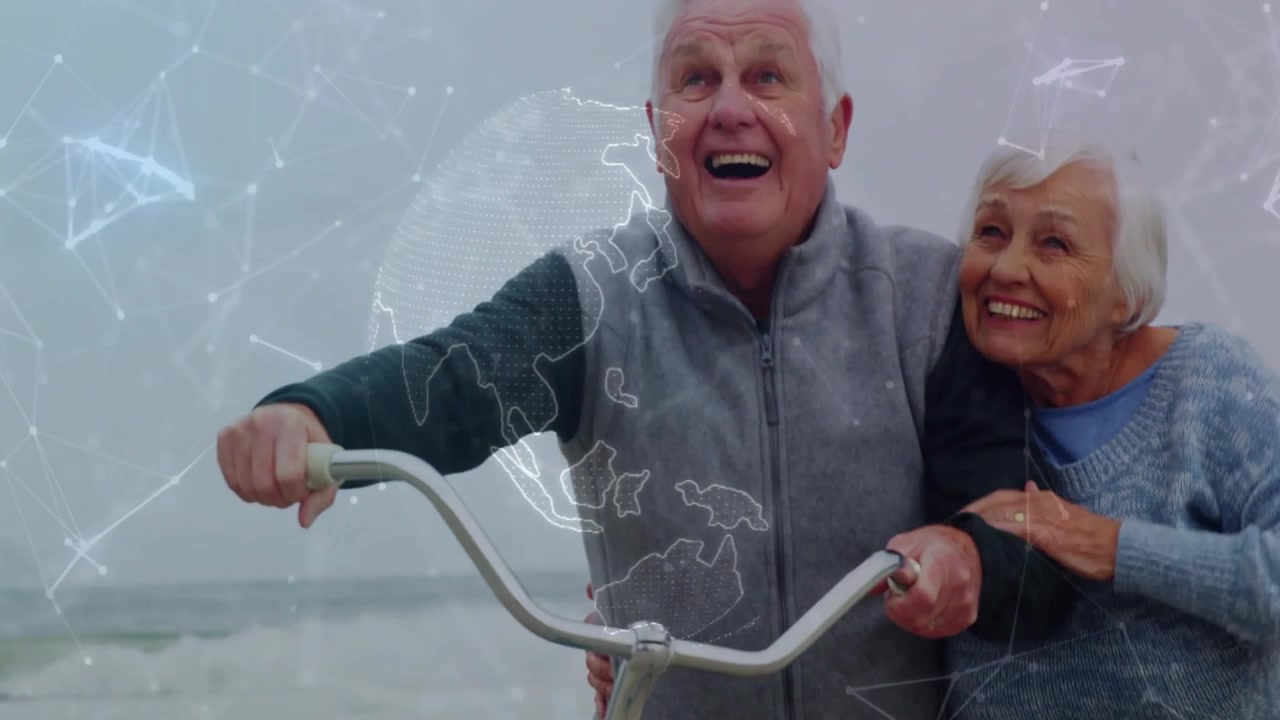 Pareja de ancianos caminando por la playa sosteniendo una bicicleta, la mujer señalando hacia arriba mientras ve el mar con una superposición tecnológica de globo que se desvanece.