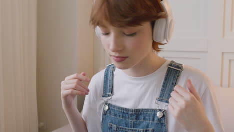 close up view of girl sitting on bed wearing headphones and moving her head to the beat of the music