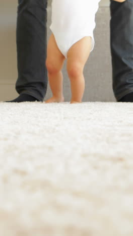 father helping baby to walk across rug