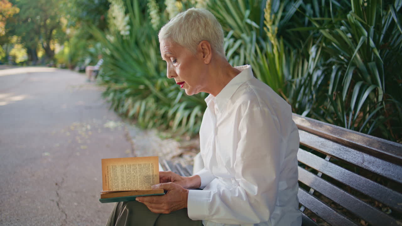 Elderly lady enjoying novel resting sunny morning in green park. Stylish senior