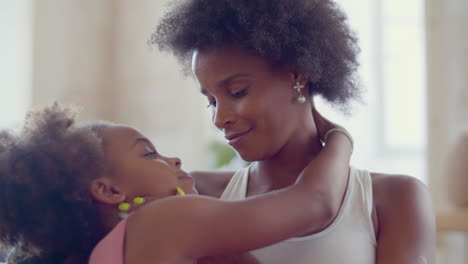 loving black woman embracing and kissing her daughter at home