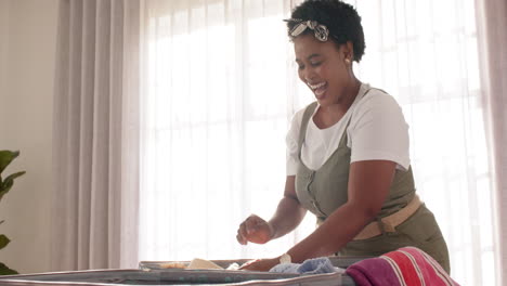 African-American-woman-packing-suitcase-for-vacation,-with-copy-space,-at-home