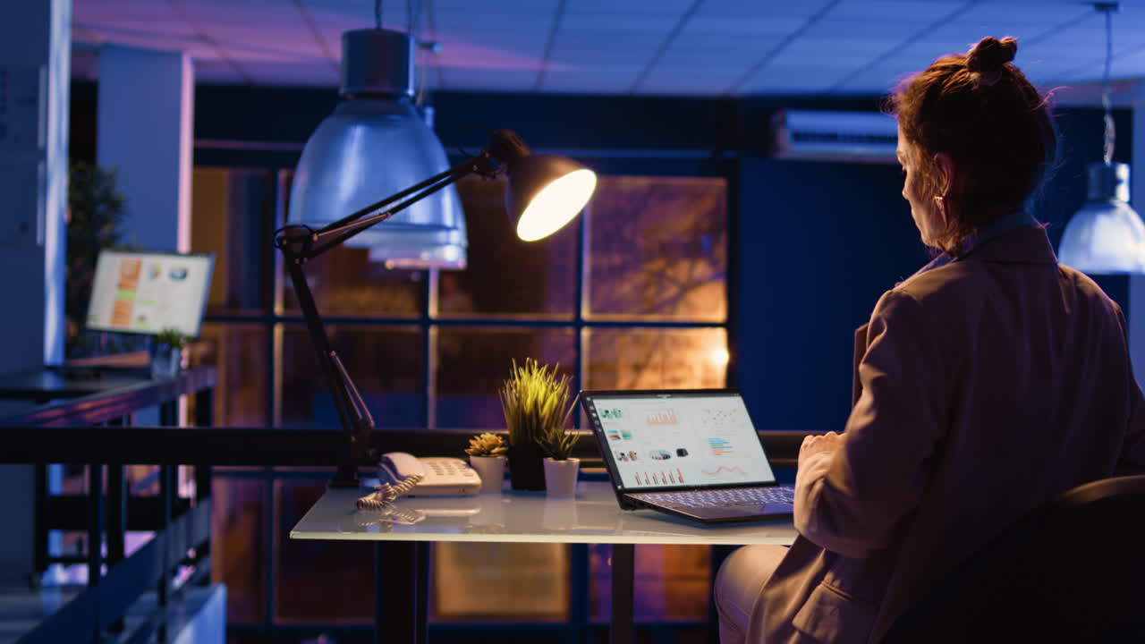 Woman working on laptop at desk in office at night