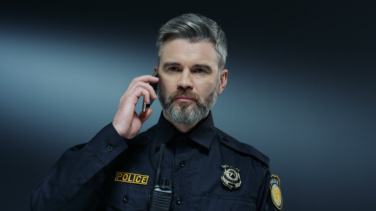 잘생긴 회색 머리 경찰관이 휴대전화로 말하고 몇 가지 중요한 결정을 내립니다.