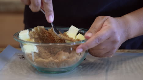 Mezclando-Azúcar-Moreno-Y-Mantequilla-Con-Un-Tenedor-En-Un-Recipiente-De-Vidrio---Manos-Negras-Preparando-Una-Golosina