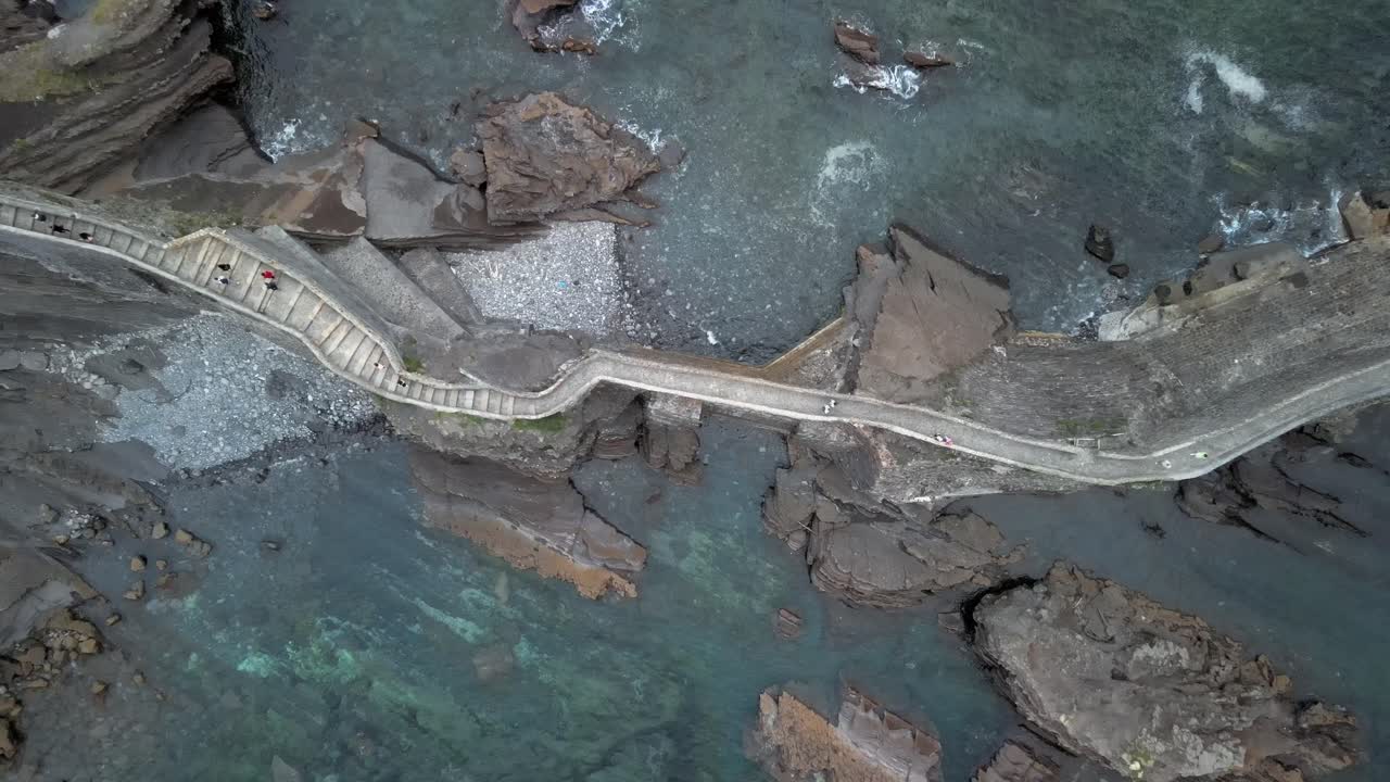 Stairway path leading to Gaztelugatxe island in rocky ocean, ascending bird's eye view, Basque Spain