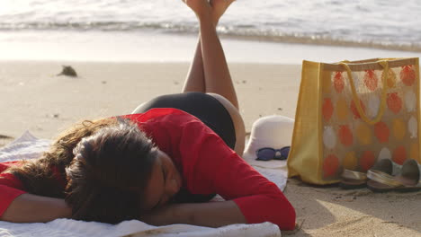 latino girl lying down relaxes in fresh summer breeze on beach sands, static shot