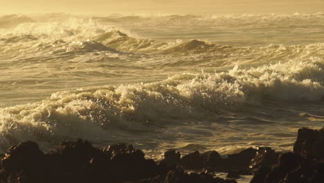 rough sea waves crashing on rocky shoreline during golden afternoon - close up pan shot