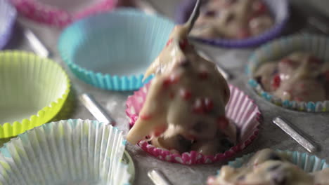 scooping muffin batter with tasty fruit into colorful wrappers in metal baking tray close up