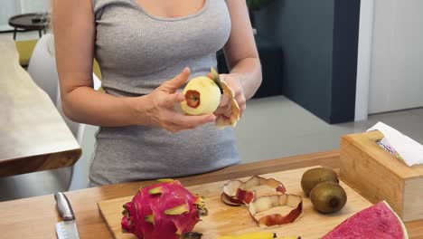 mujer pelando una manzana en una cocina con otras frutas