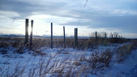 Cold-winter-sunset-seen-through-fence-on-Alberta,-Canada-grasslands