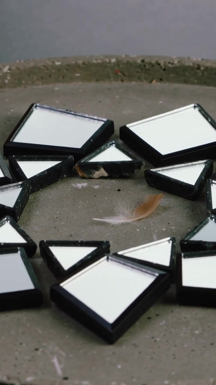 Vertical video: Shifting camera upward and closer revealing mirrors and feather on concrete tray