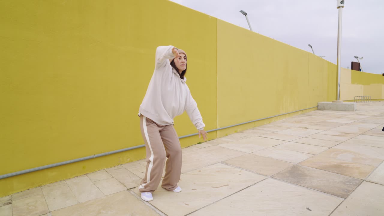 Woman dancing in streetwear against a yellow wall