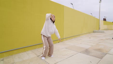 woman dancing in streetwear against a yellow wall