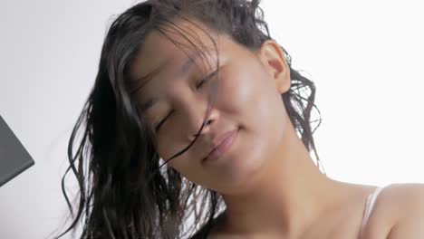 고립된 흰색 배경으로 머리를 말리기 위해 헤어드라이어를 사용하는 아름다운 젊은 아시아 여성
