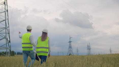 la vista desde la parte trasera: un grupo de ingenieros en una central eléctrica de alto voltaje con una tableta y dibujos caminan y discuten un plan para el suministro de electricidad a la ciudad. transporte de energía limpia renovable.