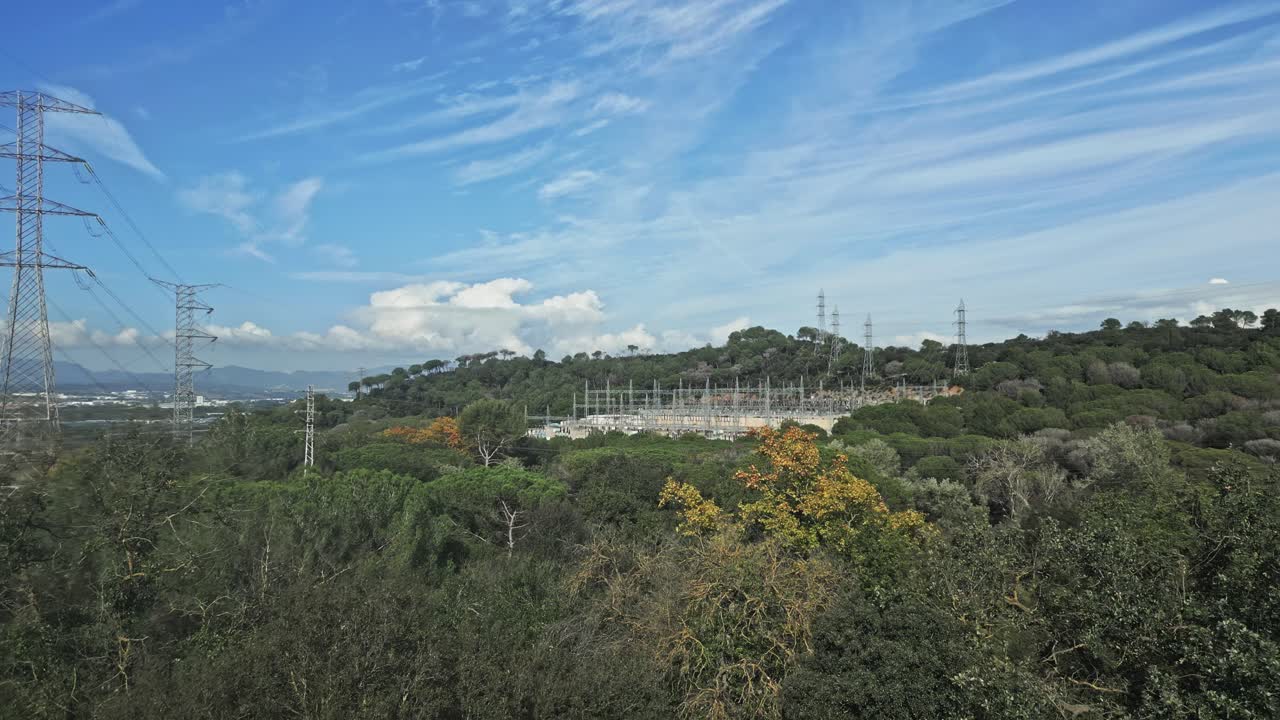 Lush vegetation surrounds an electrical substation, showcasing the integration of industrial infrastructure within a natural environment, under a vibrant blue sky