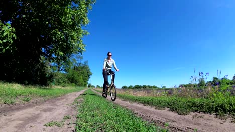 una mujer joven montando una bicicleta de época a lo largo de una carretera rural en un pueblo