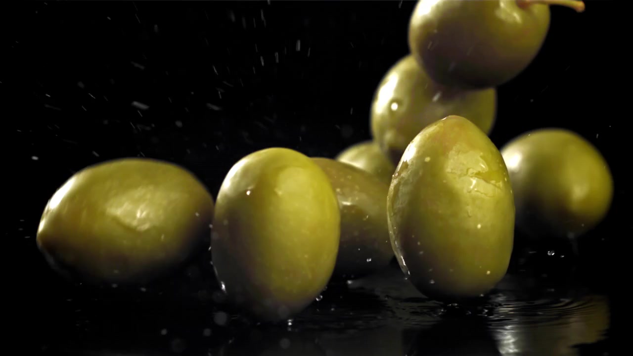 Olive verdi che cadono e schizzano su sfondo nero al rallentatore.