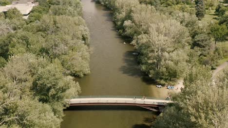 Aerial-flyover-Boise-River-with-bridge,-then-pan-up-to-reveal-Rocky-Mountains