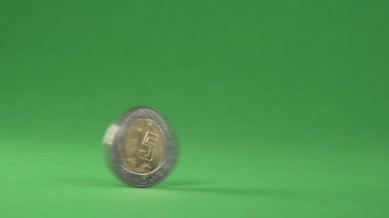 una moneda mexicana de 5 pesos girando rápidamente sobre un fondo cromático