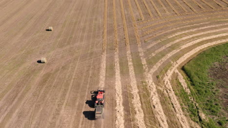 A-Tractor-At-Work-Baling-Hay-At-The-Farm-In-Saskatchewan,-Canada-On-A-Sunny-Day---aerial-drone