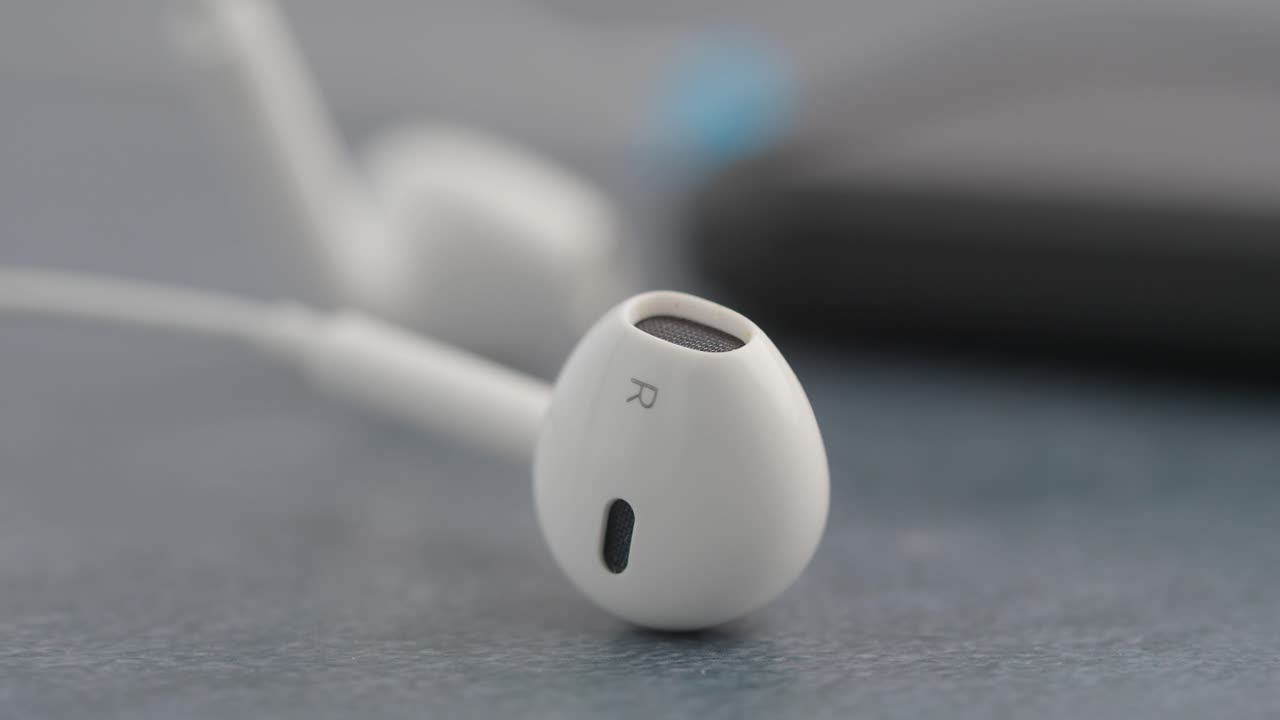 Nærbillede af en hvid in-ear høretelefon og en sløret smartphone