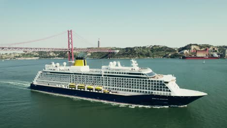 cruise ship sailing past the tagus river bridge in lisbon, portugal