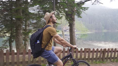 man riding bike in forest against lake view.