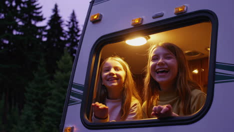 two happy girls waving from an rv window at night