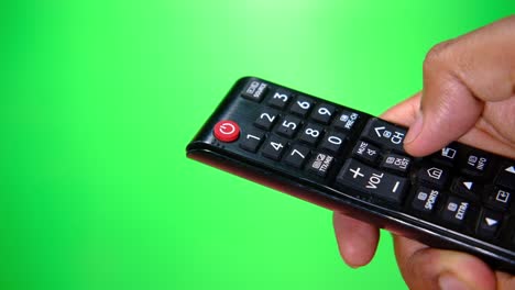 hand holding a black tv remote control on a green screen background