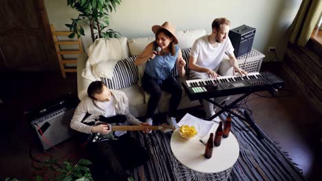 high angle view of musical band rehearsing in home studio. active emotional young people are playing musical instruments keyboard and guitar and singing.