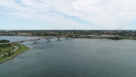 A-drone-captures-Fort-Erie-Peace-Bridge-on-a-cloudy-summer-day,-connecting-Fort-Erie-to-Buffalo,-flying-over-the-blue-waters-with-cities-in-the-background