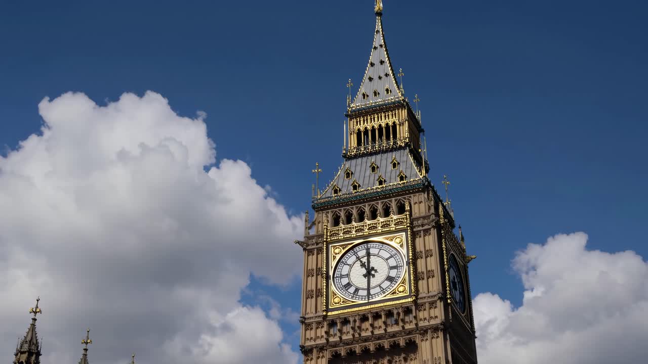 Low-angle video shot of a clock tower against a blue sky with clouds, capturing the grandeur