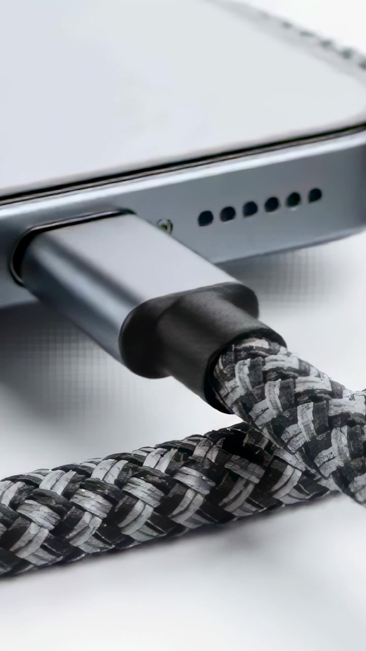 Vertical video: Reframing camera moving woven cable and phone plug closer on tabletop, showing port