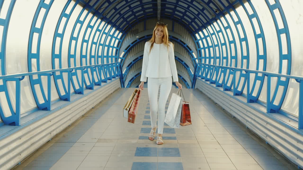 현대적인 유리 전환 또는 터널에 대해 이야기하는 쇼핑백을 들고 있는 스테디캠 샷 세련된 젊은 여성
