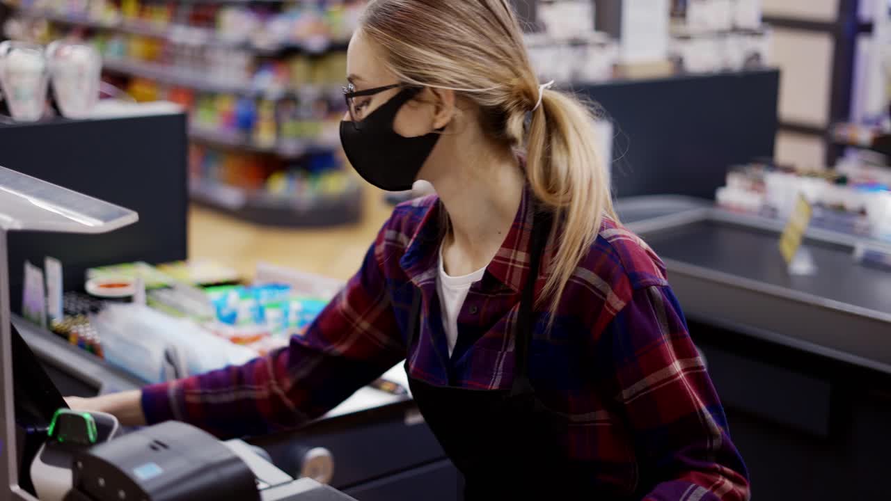 Female cashier in a protective mask pierces the products with the scanner in slow motion