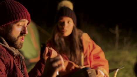 bearded man sharing a story with his friends around camp fire